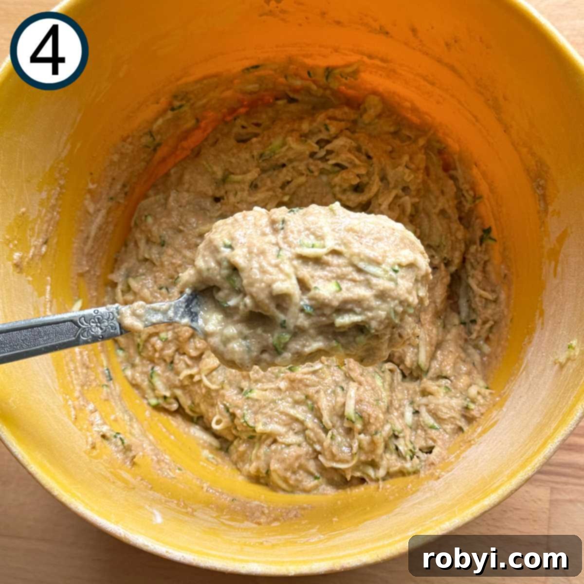 Spoon lifting thick zucchini batter out of bowl.