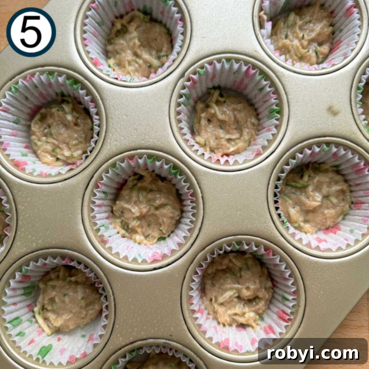 Small amount of zucchini muffin batter in the bottom of paper inserts in a muffin tin.