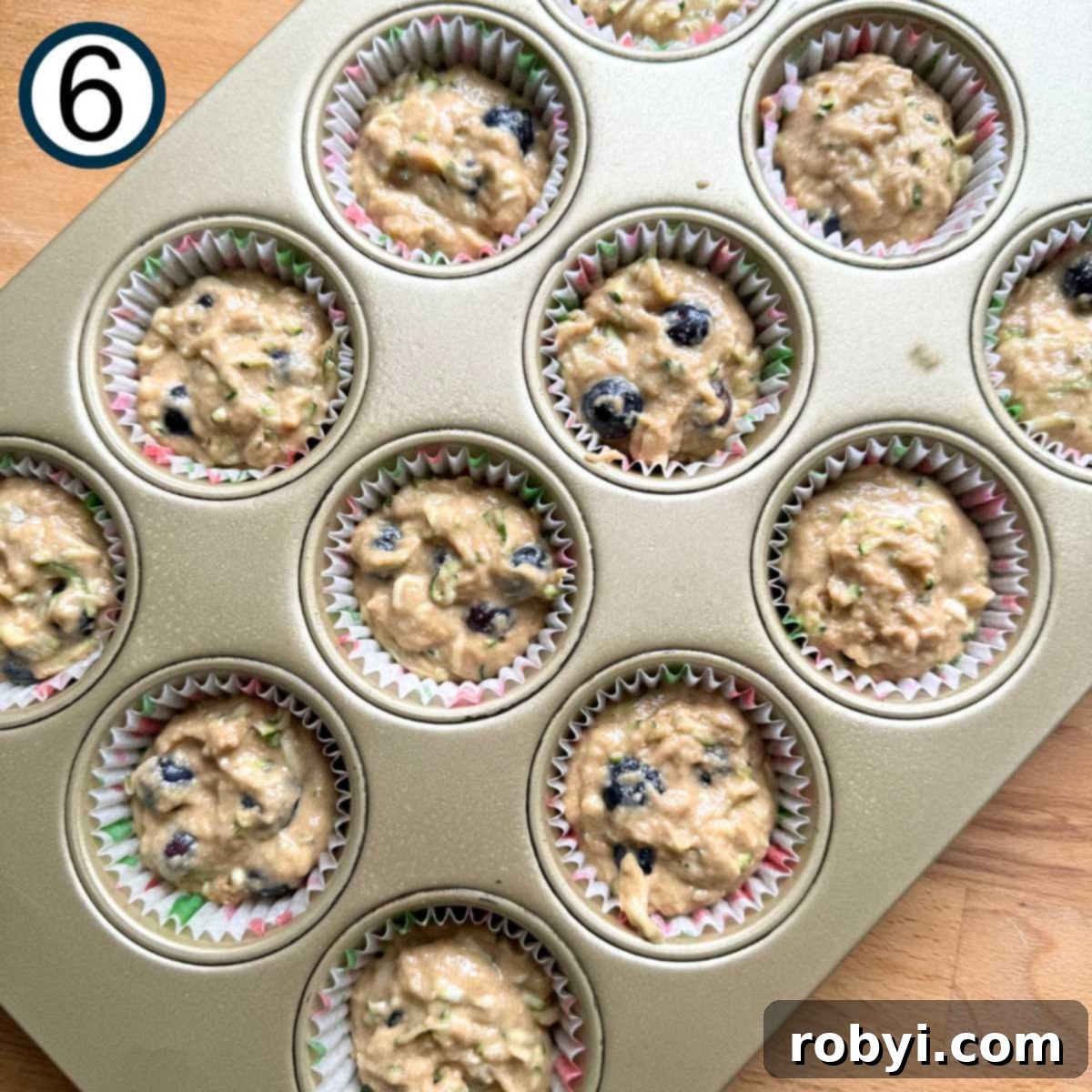 Muffin wells filled almost to the top with zucchini blueberry muffin batter.