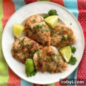 White plate with four baked chili lime chicken using tajin seasoning with lime wedges and cilantro.