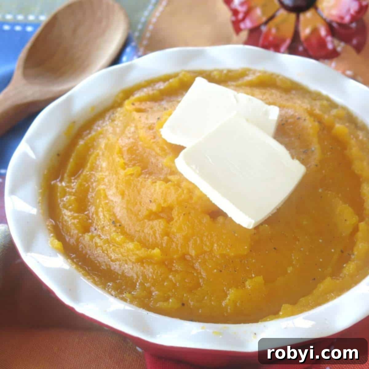 A serving bowl filled with mashed butternut squash, cooked in a crock-pot, garnished with pats of butter.