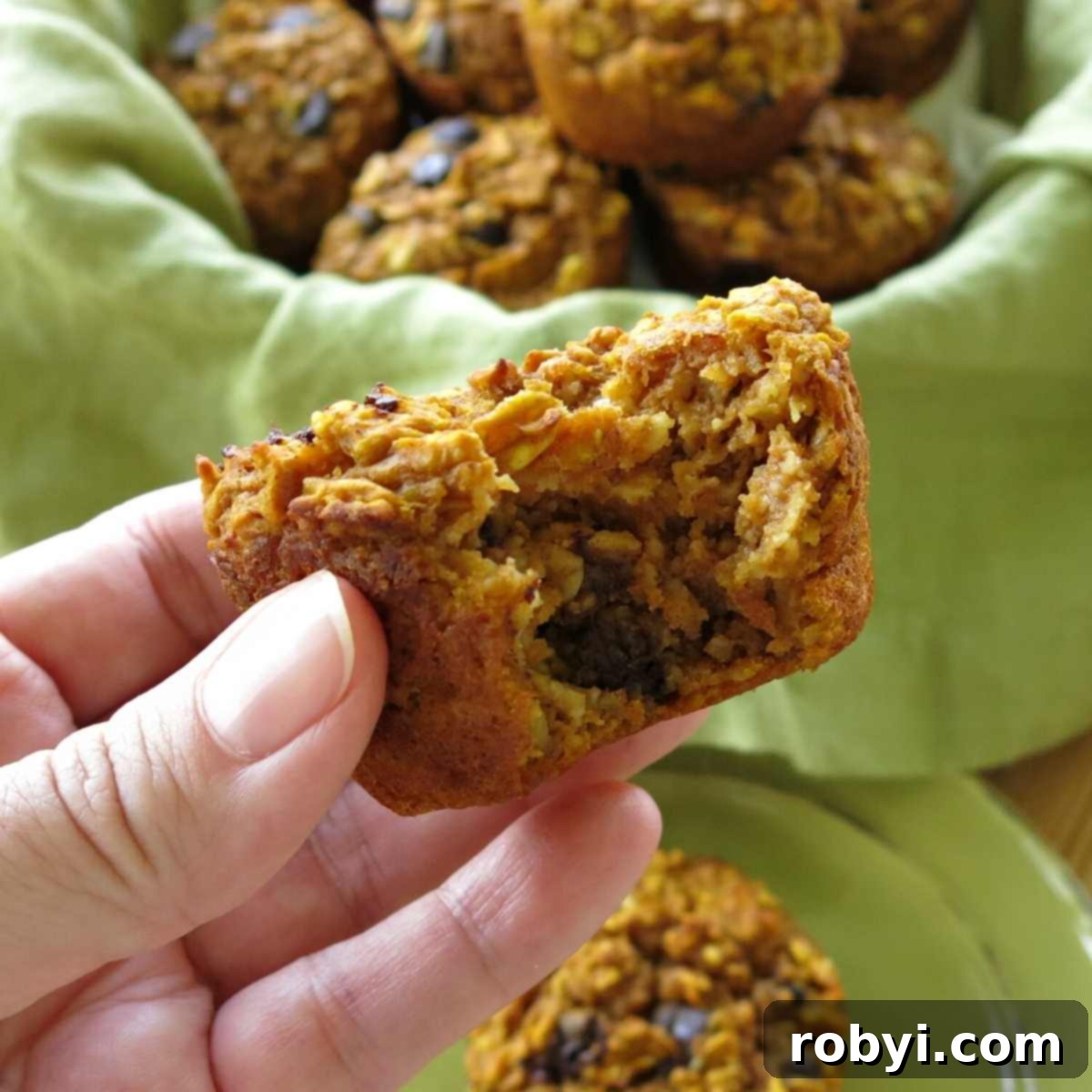 Hand holding a gluten-free oatmeal pumpkin muffin with a bite removed, showcasing its delicious texture.