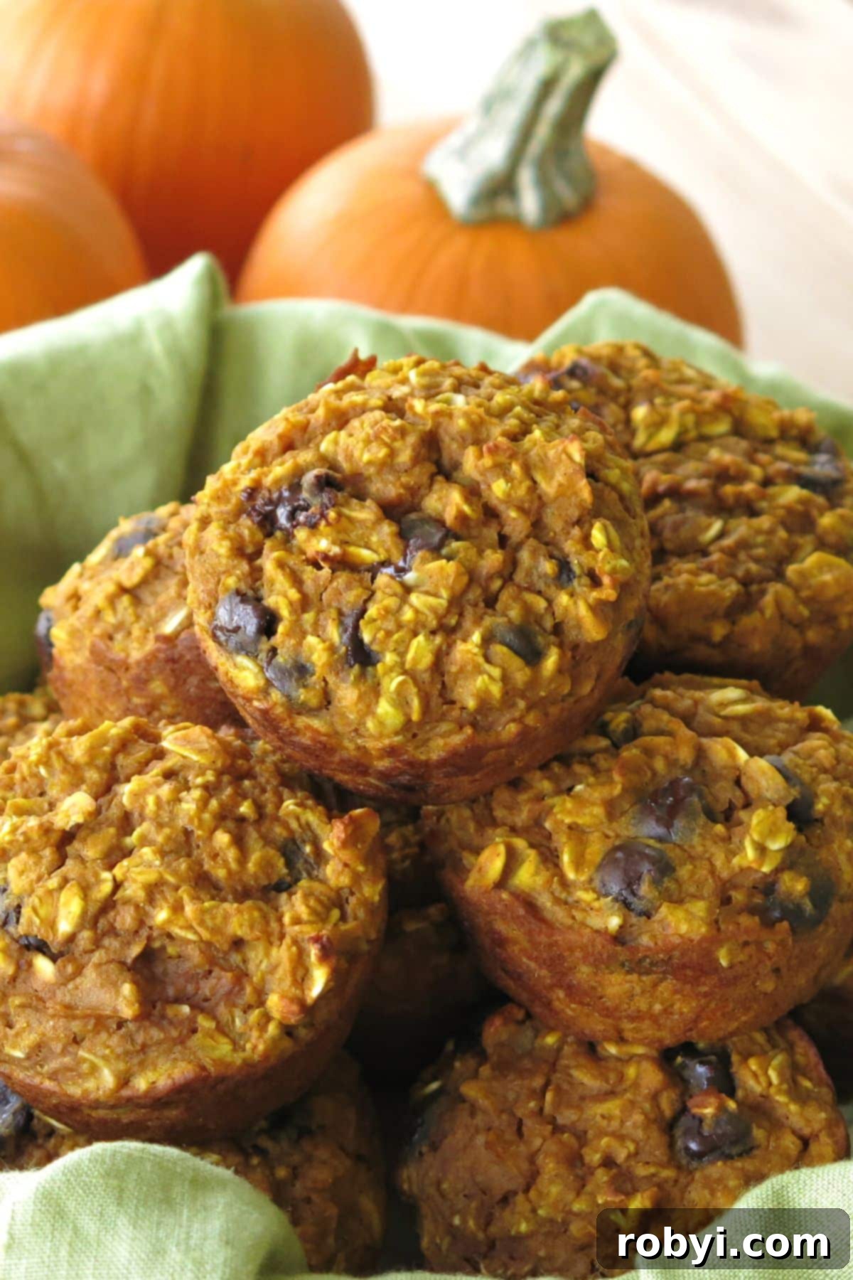 Baked oatmeal pumpkin cups piled on top of each other with pumpkins behind them, ready to be enjoyed.