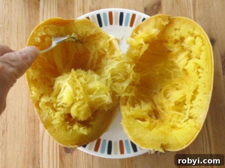A fork being used to remove spaghetti squash strands from the cooked gourd, showcasing its pasta-like texture.