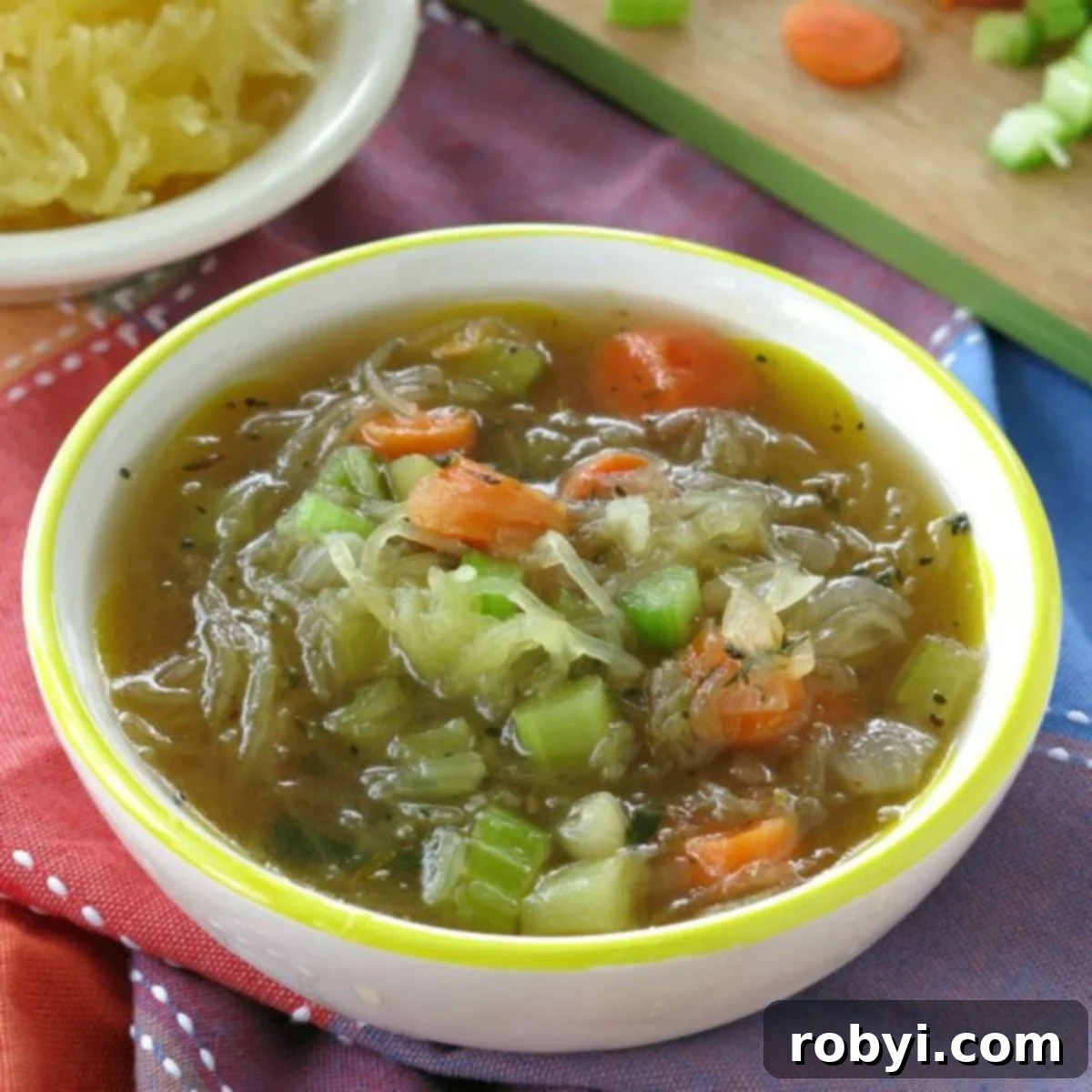 Easy spaghetti squash soup in a bowl with a bowl of spaghetti squash and cut vegetables behind it.