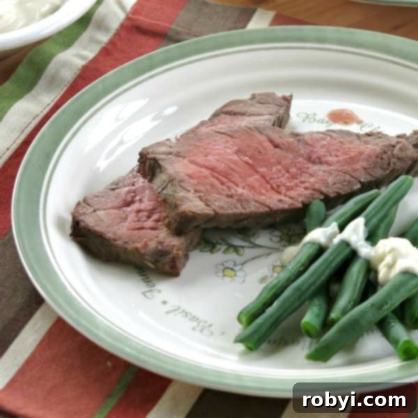 The Ultimate Oven-Baked London Broil 5 Two slices of medium-rare London Broil on a plate next to green beans.