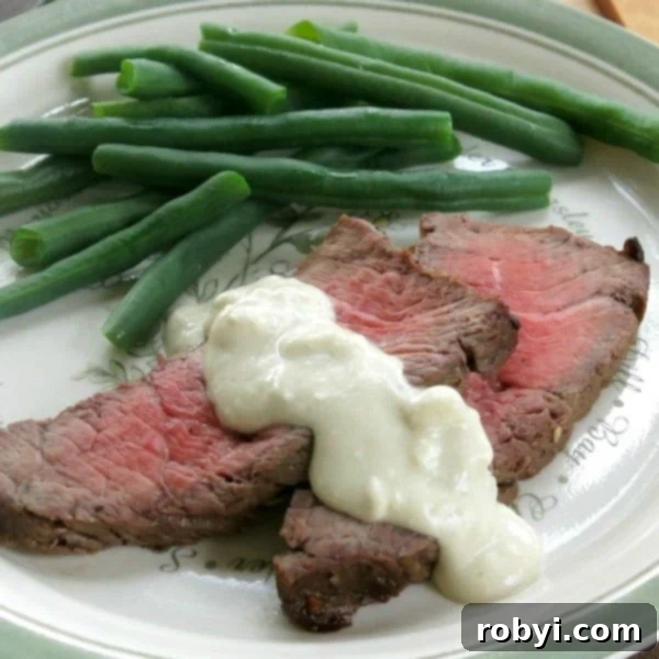 The Ultimate Oven-Baked London Broil 8 London Broil topped with a delicious Blue Cheese Sauce, served on a plate next to green beans.