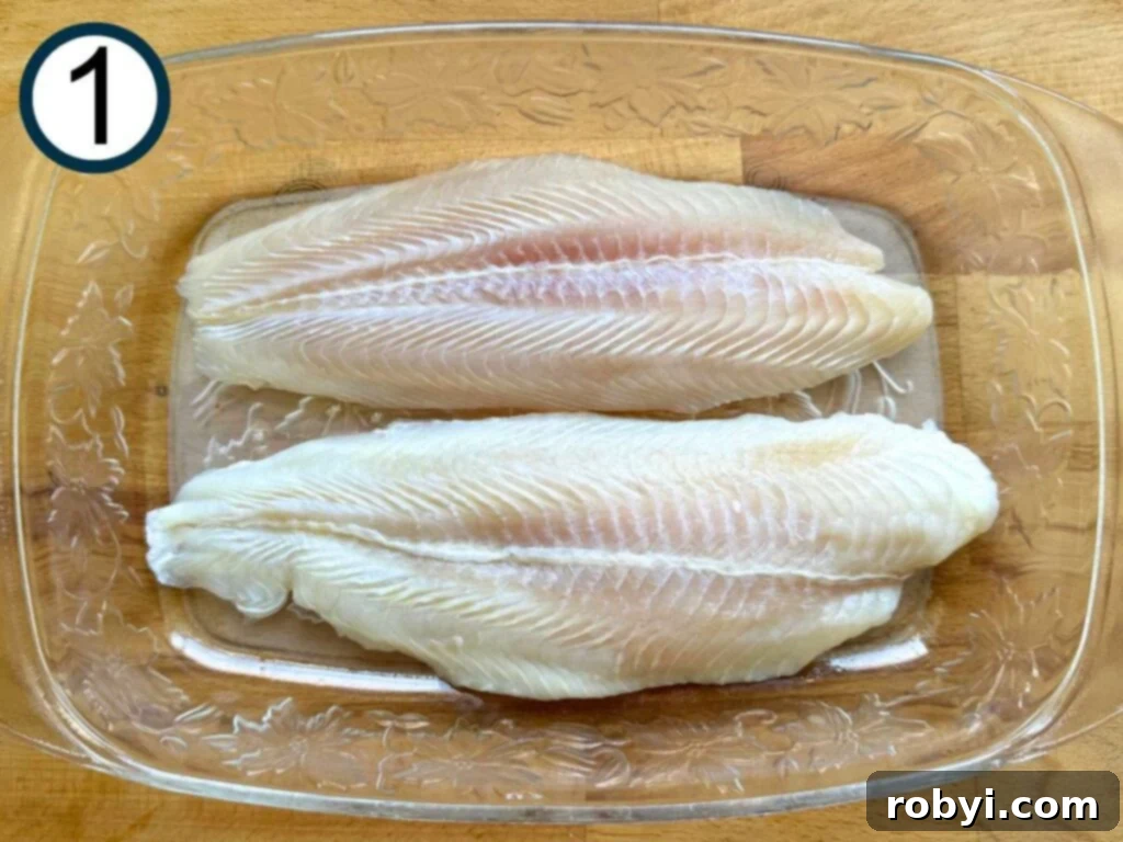 Two uncooked basa fish fillets in a glass baking dish, lightly coated with cooking spray.