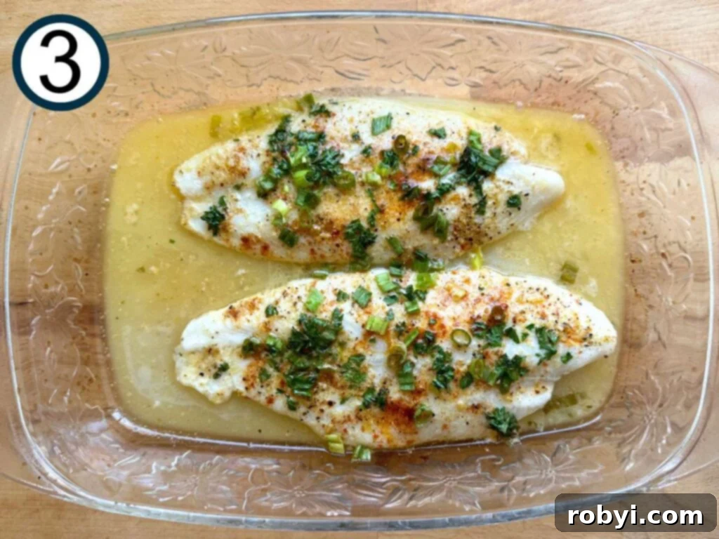 Two cooked lemon baked basa fillets in a glass baking dish, showing flaky, opaque flesh.