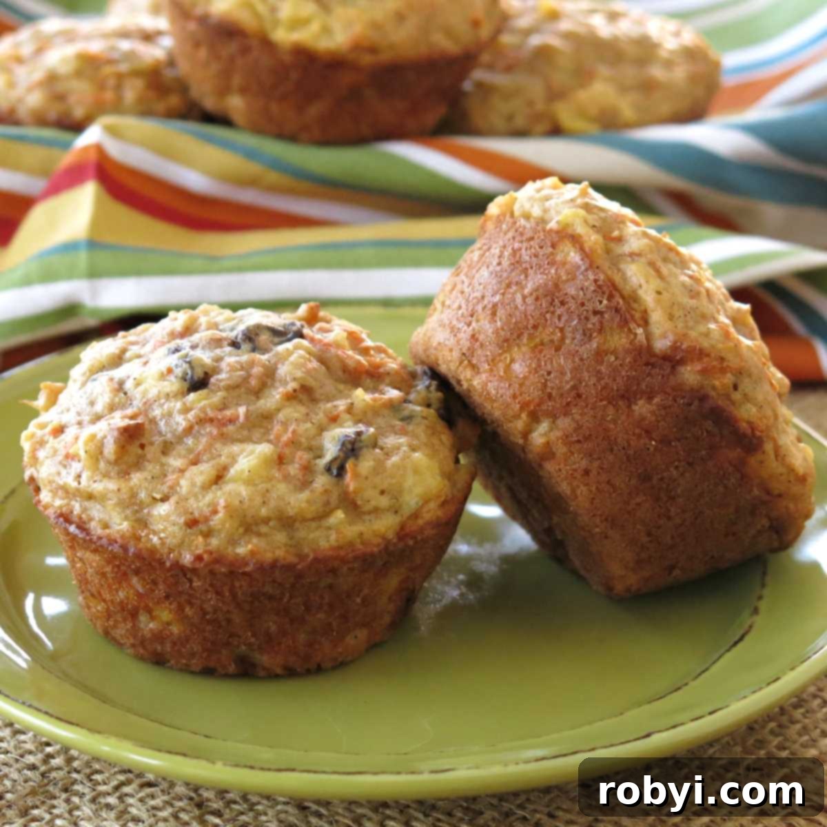 Two healthy pineapple carrot muffins on a plate with more in a basket behind them. These muffins are golden brown and speckled with visible carrot shreds and nuts.