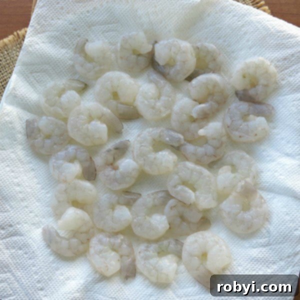 Raw, peeled, deveined shrimp with tails removed, neatly arranged on a paper towel, ready for cooking.