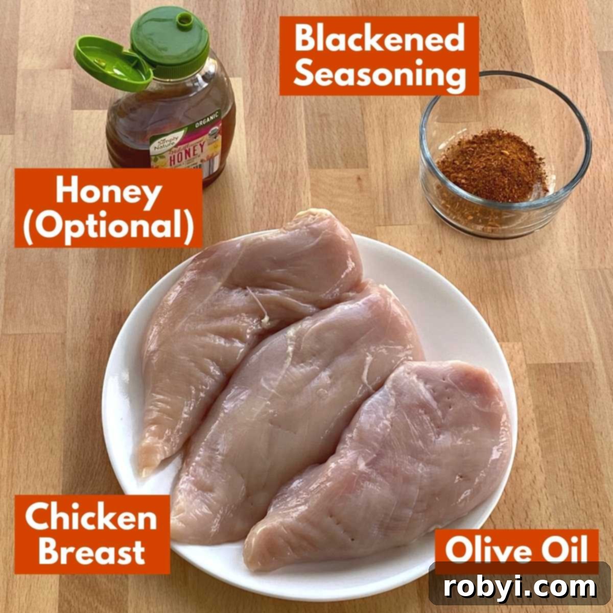 Spicy Oven-Roasted Chicken Breasts 3 Clearly labeled ingredients for baked blackened chicken laid out on a rustic wooden table, including chicken breasts, a spice blend, honey, and olive oil.