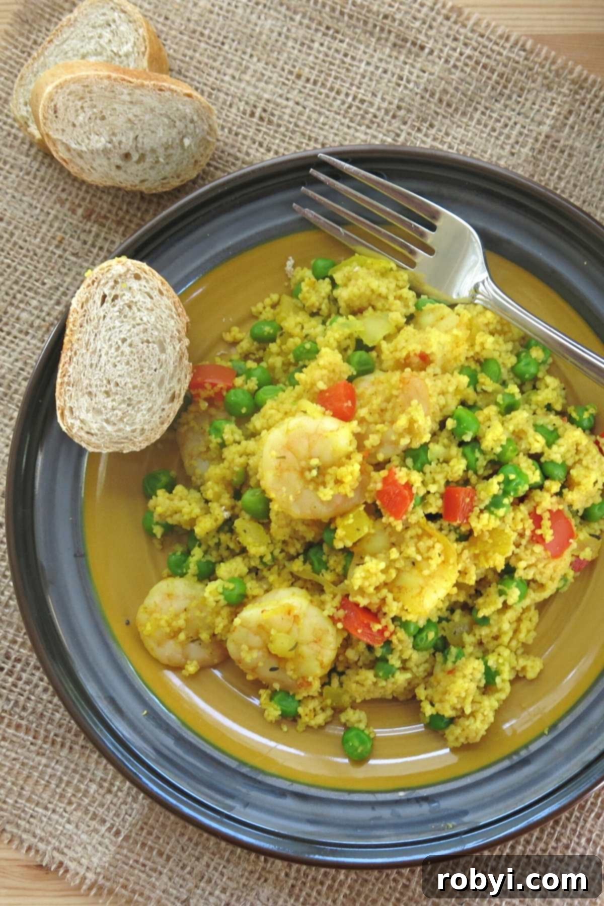 A serving of one-pot shrimp couscous paella on a plate, garnished with fresh parsley and accompanied by a slice of crusty bread.