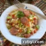 Cajun cauliflower rice with andouille sausage in a bowl with a fork resting on the edge.