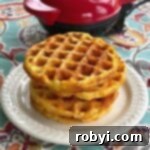 Cauliflower Waffles stacked on a plate in front of a waffle maker.