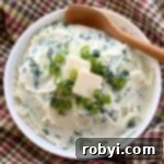 Creamy cauliflower colcannon topped with butter and green onions in a white bowl with a spoon.