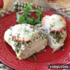 Baked pesto chicken with tomatoes and mozzarella cheese cut in half on on a red plate with arugula and a fork in background.