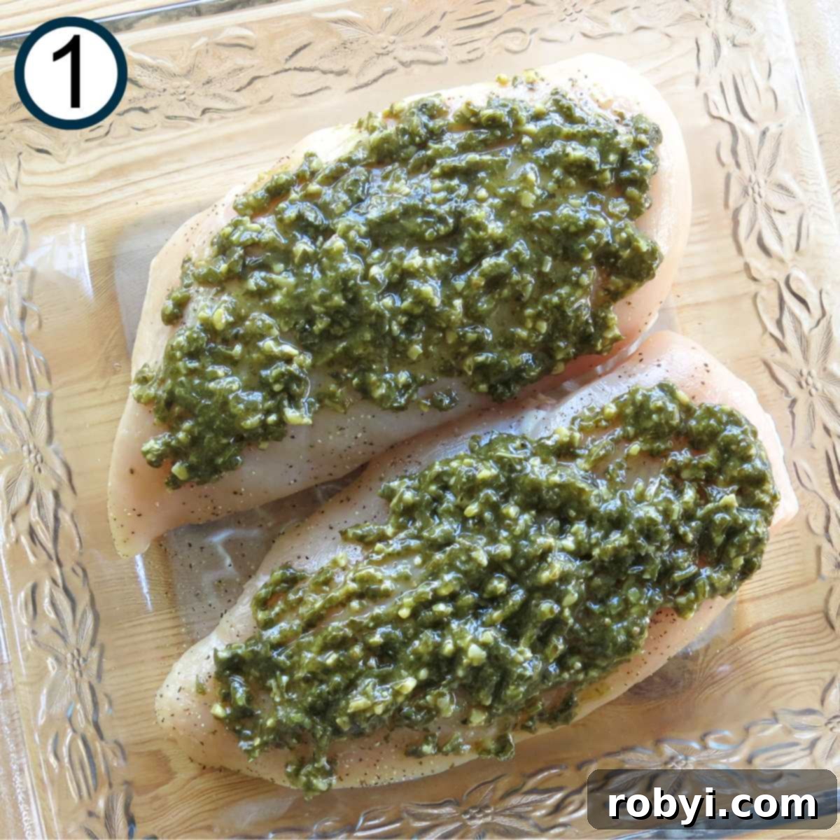 Two boneless skinless chicken breasts topped with pesto in a glass baking dish.
