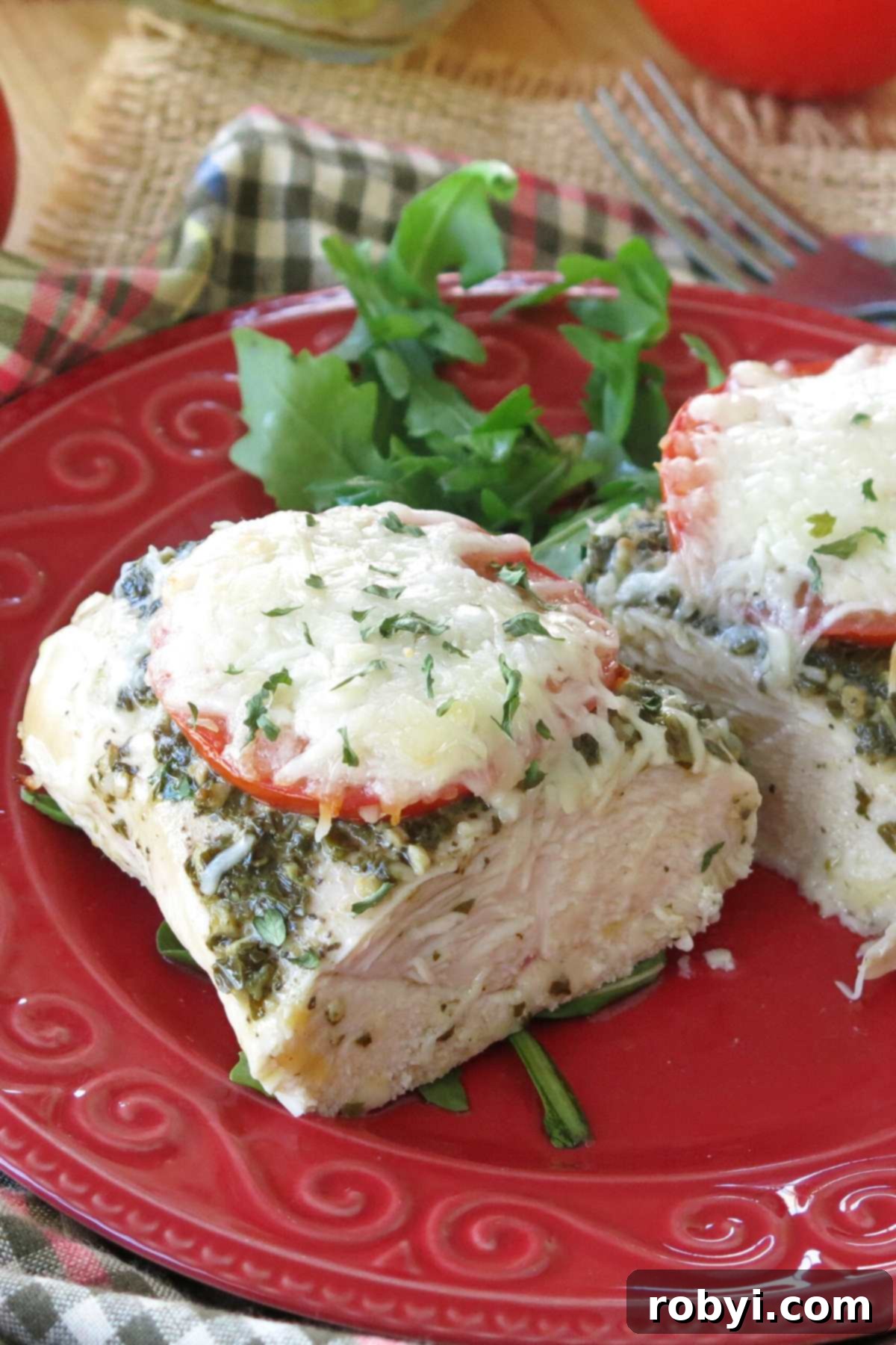 Close-up of juicy center of baked pesto chicken breast on a red plate with arugula behind it.