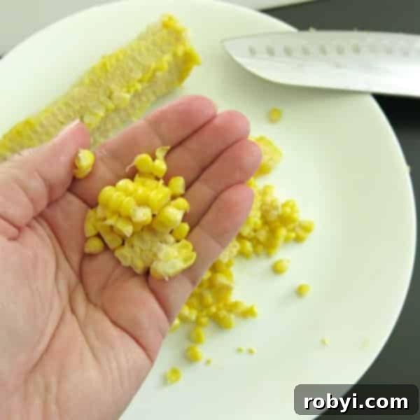 Lock in Flavor: Freezing Corn on the Cob, Husk Included 3 Hand holding previously frozen corn kernels with a cob and knife on a cutting board