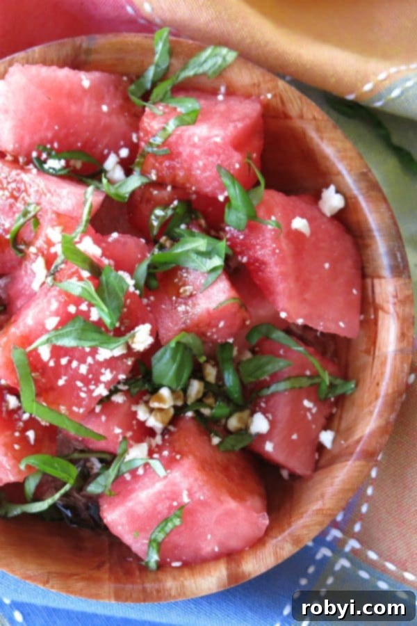 A bowl filled with refreshing Watermelon Salad, garnished with fresh basil, crumbled feta cheese, and a glossy balsamic glaze.