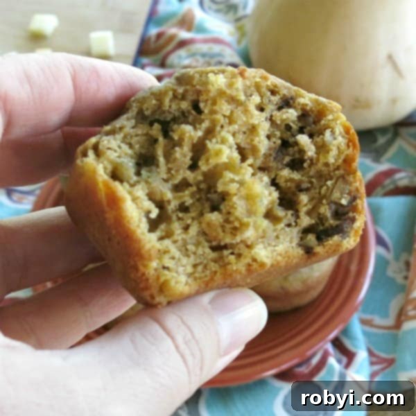 A hand holding a butternut squash apple muffin with a bite removed, showing the moist texture and ingredients.
