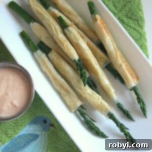 Phyllo wrapped asparagus on a platter next to aioli in a cup.