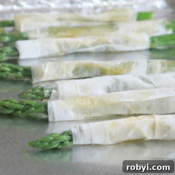 Asparagus wrapped in phyllo dough on a baking sheet.