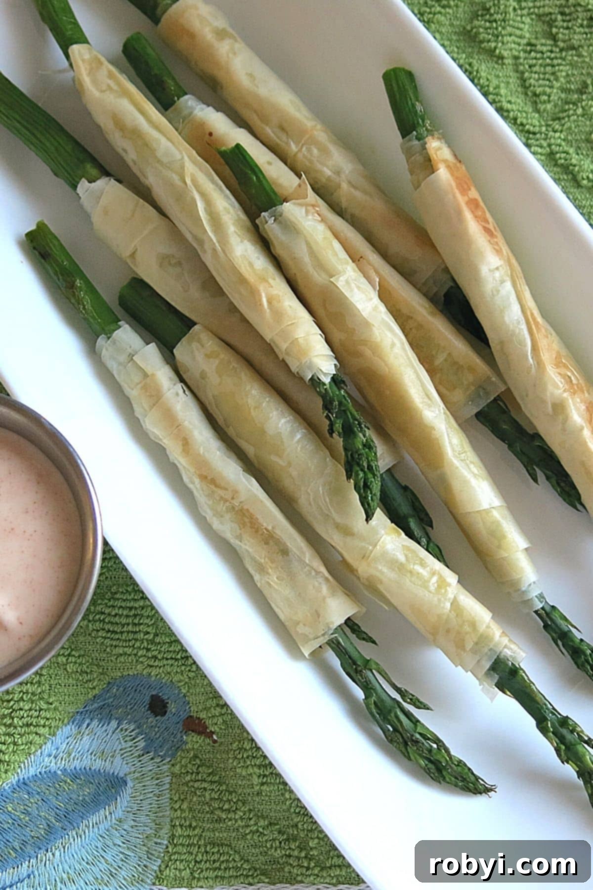 Phyllo wrapped asparagus on a platter next to aioli dipping sauce.