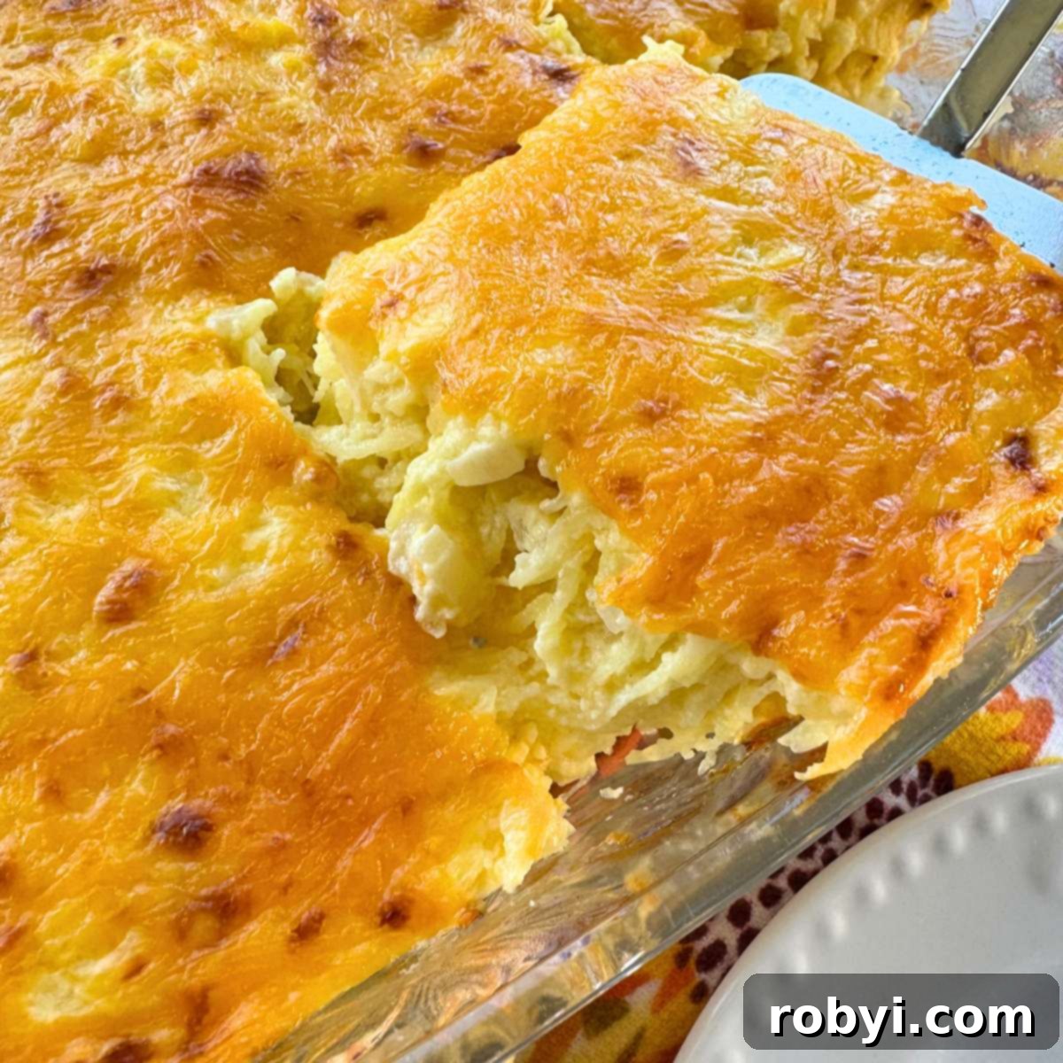 A serving of golden-brown spaghetti squash au gratin being scooped out of a bubbling casserole dish, highlighting its cheesy top and tender strands.