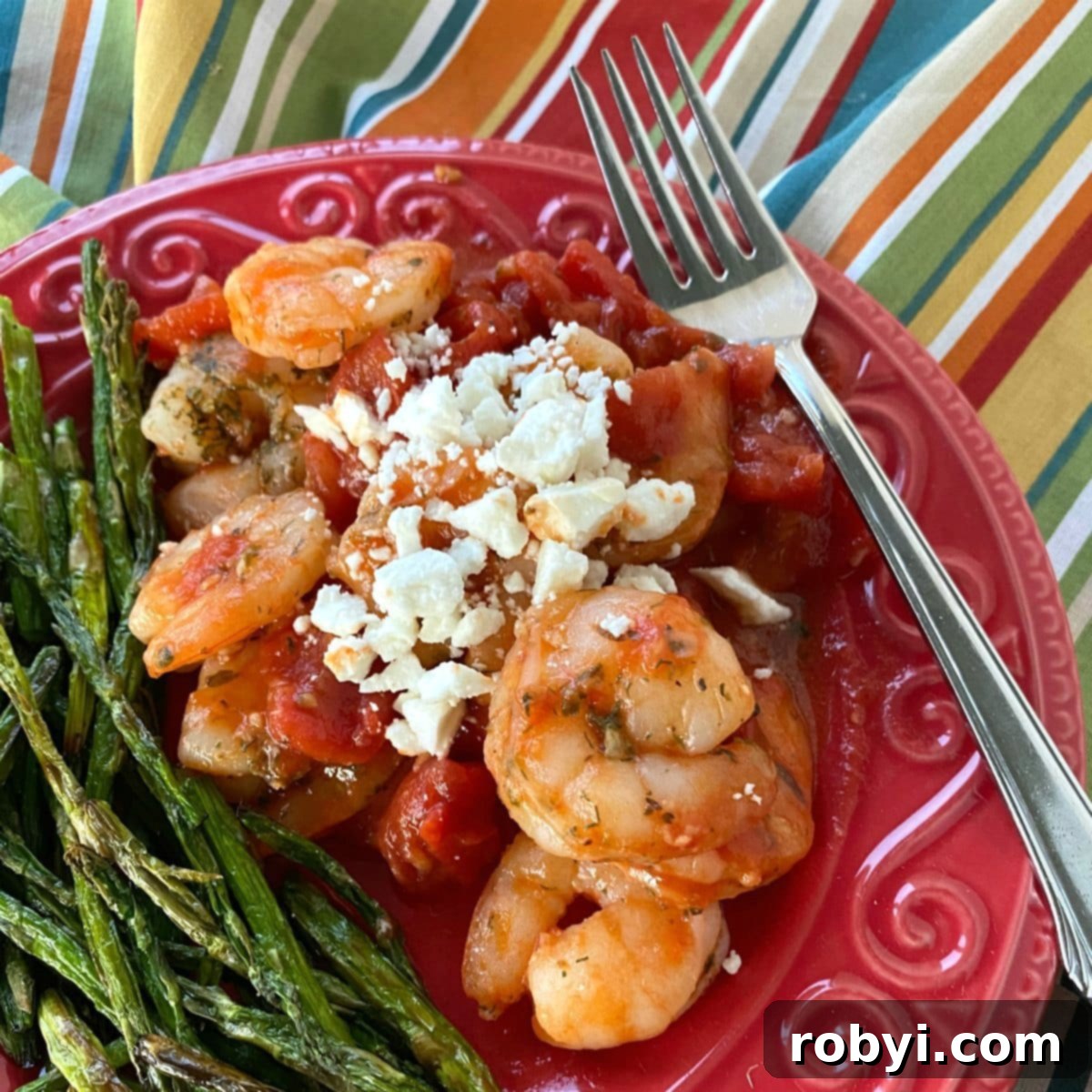 Sizzling Skillet Greek Shrimp with Burst Tomatoes and Crumbled Feta 2 Serving of Greek shrimp with tomatoes and feta cheese on plate next to asparagus.