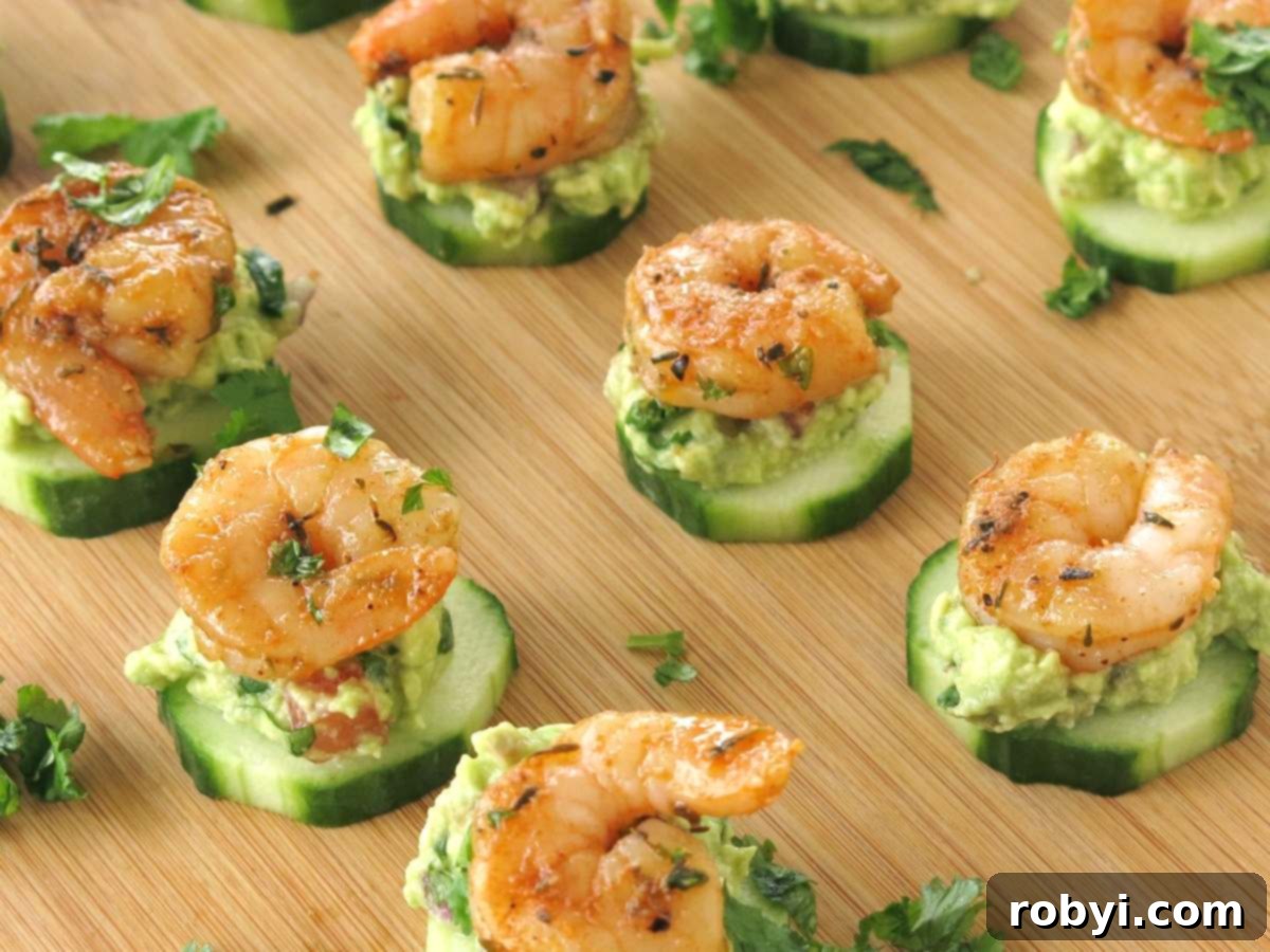 Lines of shrimp layered on top of guacamole on a slice of cucumber.