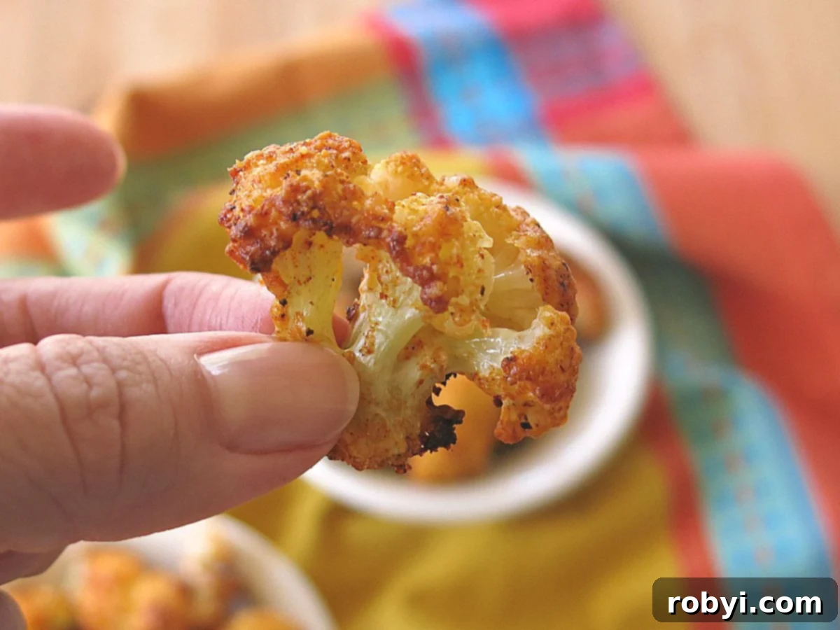 Fingers holding a Parmesan Cauliflower Bite over a bowl with more.