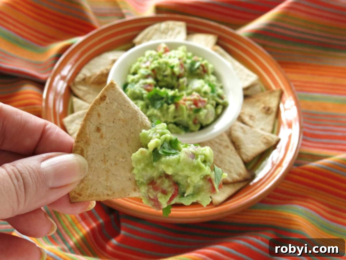 Fingers holding a low-carb flour tortilla chip with guacamole on it.