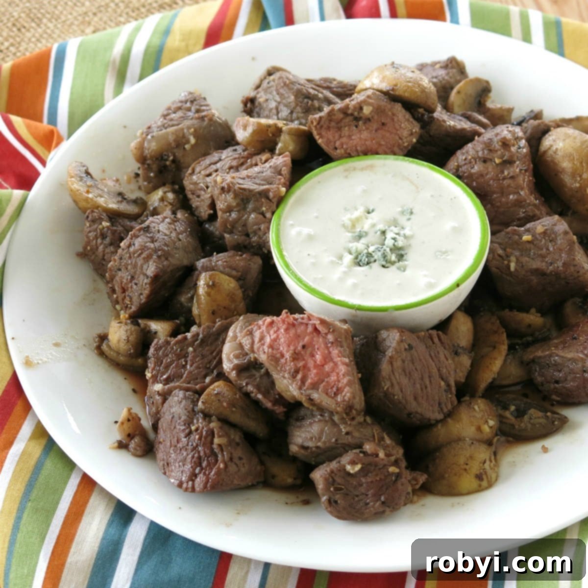 Air Fryer Steak Bites on a plate with mushrooms and blue cheese dipping sauce, ready to be served.
