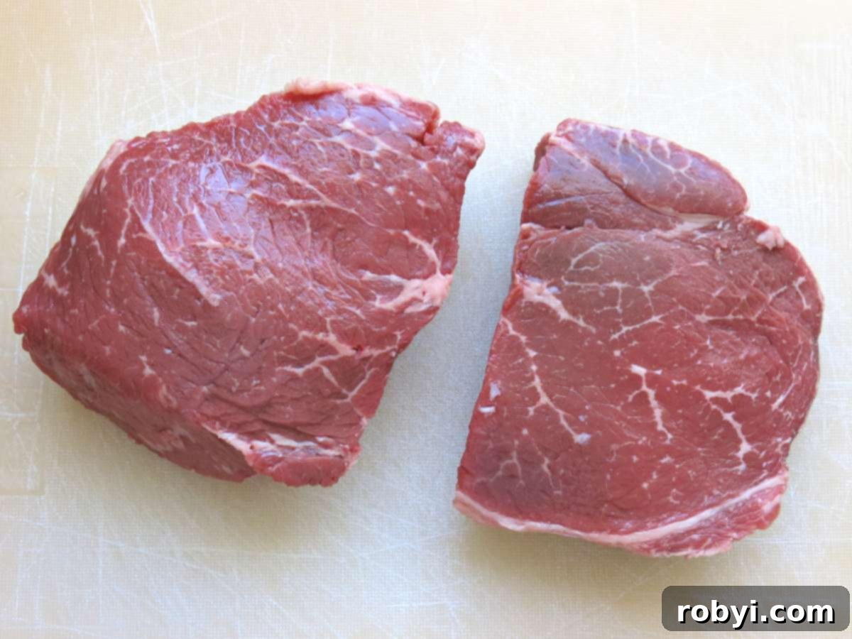 Two sirloin steak filets on a cutting board, ready to be cut into cubes.