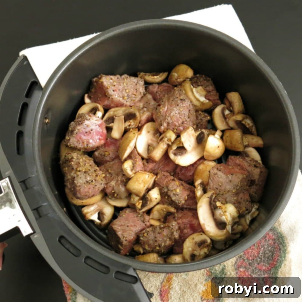 Partially cooked steak bites and mushrooms in an air fryer basket, showing initial browning.