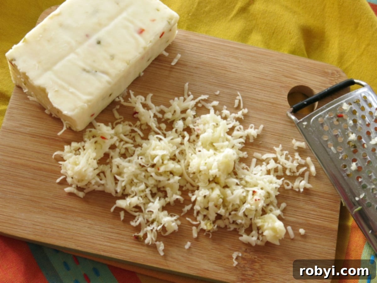 Block of Pepper Jack cheese on cutting board with shredded cheese and grater