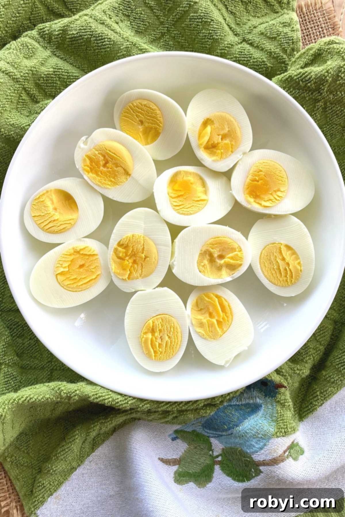 Easy Air Fryer Hard Boiled Eggs for All Models 5 A plate arranged with several halves of hard-boiled eggs, showcasing their perfectly cooked yolks, resting on a clean towel.
