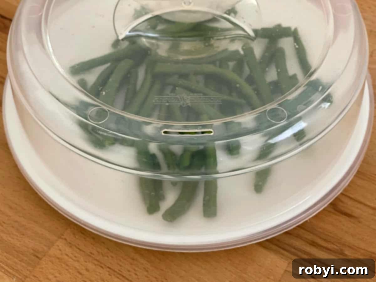 Green beans arranged on a plate covered with a microwave-safe lid, demonstrating the initial softening technique.