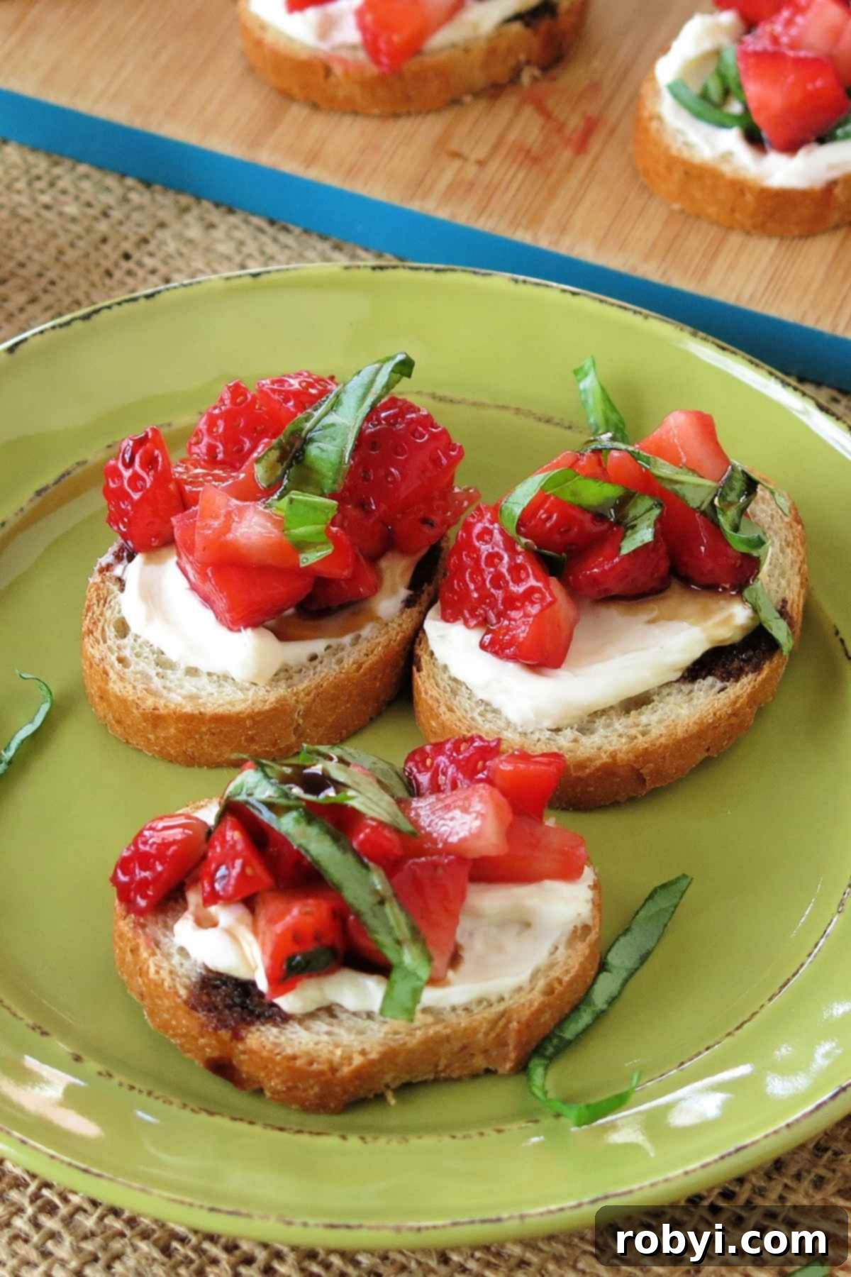 Plate with 3 slices of strawberry bruschetta cream cheese appetizer topped with basil and balsamic vinegar glaze.