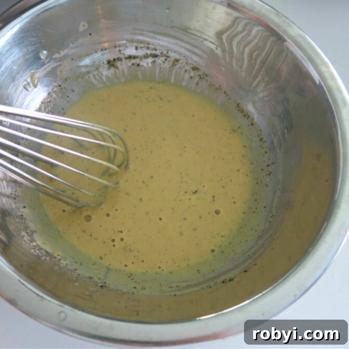 Dijon mustard and lemon sauce in a bowl, being whisked to combine.