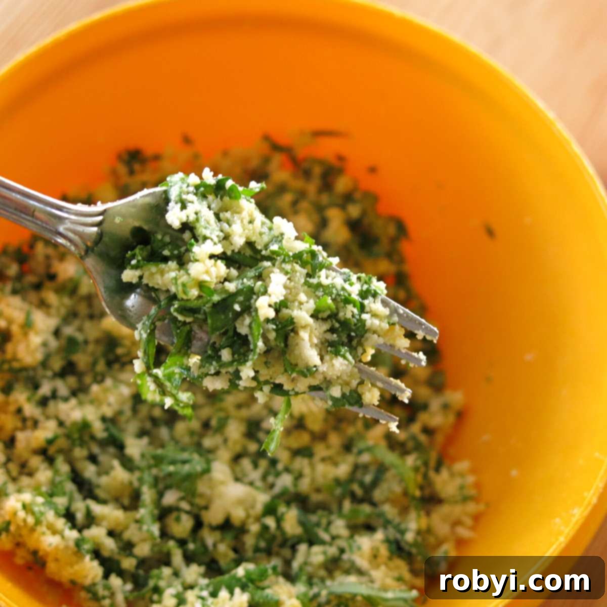 Fork mixing fresh herb and Parmesan breading ingredients in a bowl.