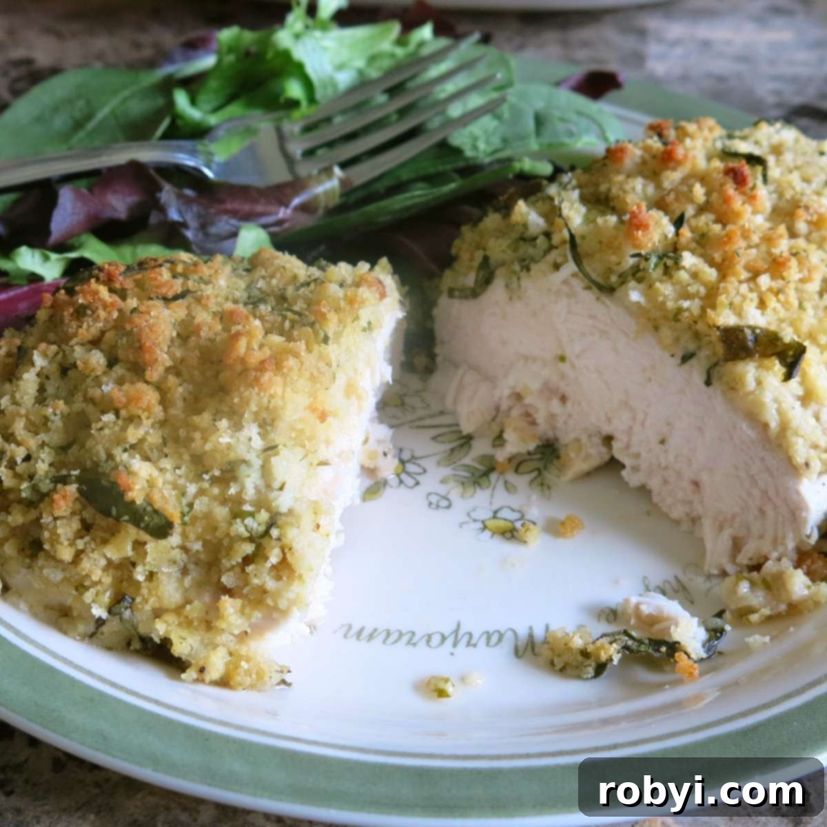Baked herb crusted chicken breast sliced in half to reveal a juicy interior on a plate.