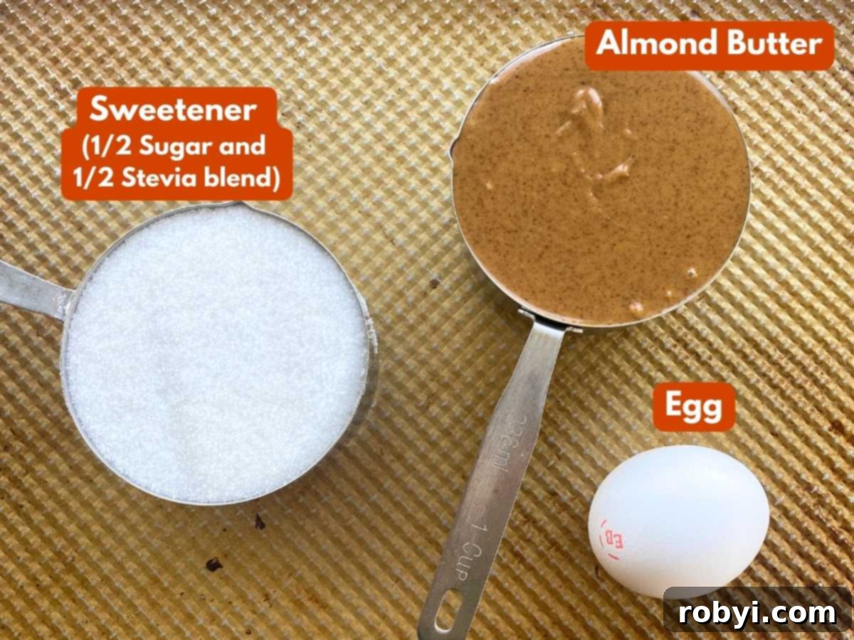 Three core ingredients for almond butter cookies in measuring cups: creamy almond butter, a blend of sugar and stevia, and a single egg.