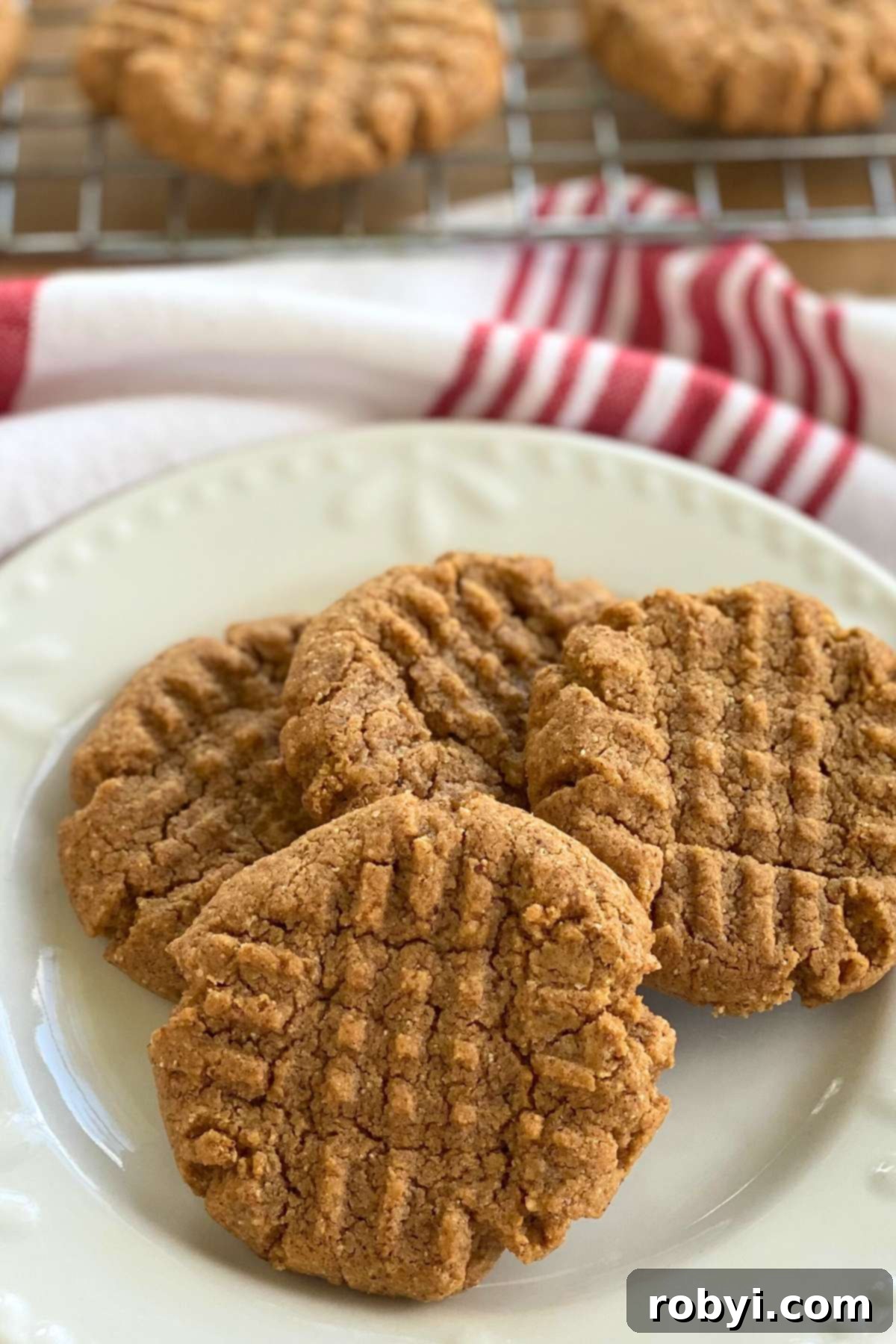 Perfectly baked gluten-free almond butter cookies cooling on a rack, with a few ready to eat on a plate.