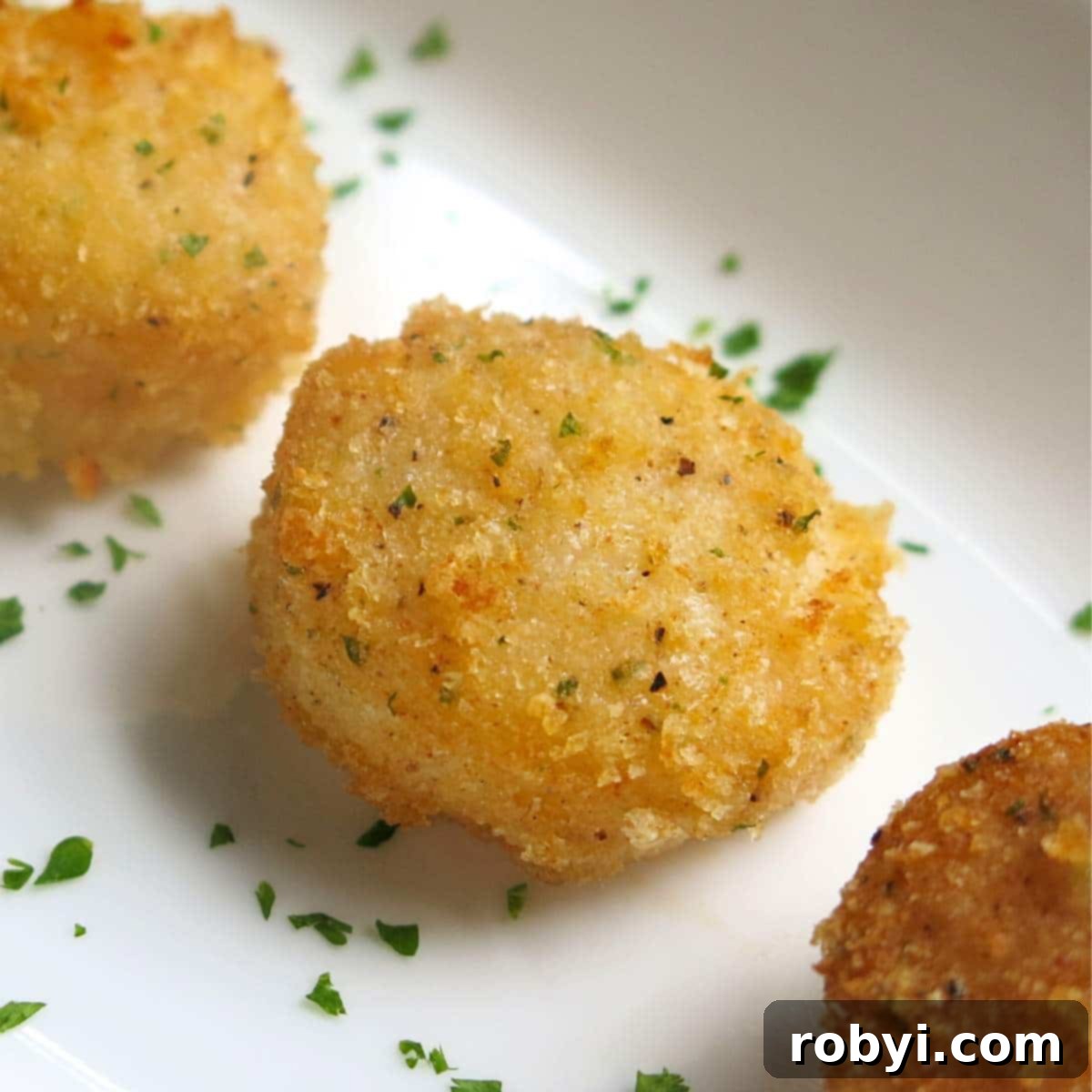 Parmesan Crusted Broiled Scallops lined up on a plate with minced parsley around them, ready to be served.