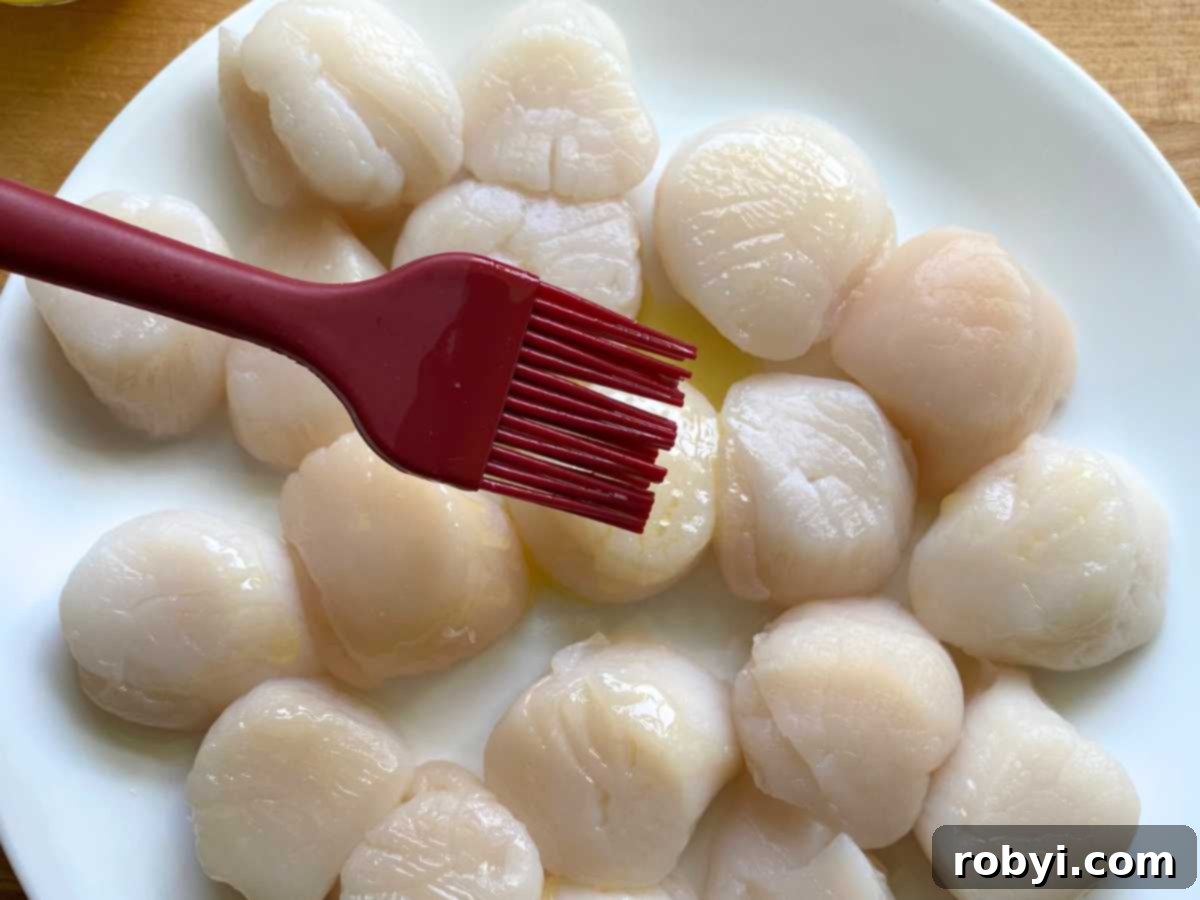 Silicone brush applying butter and olive oil mixture to sea scallops on a plate.