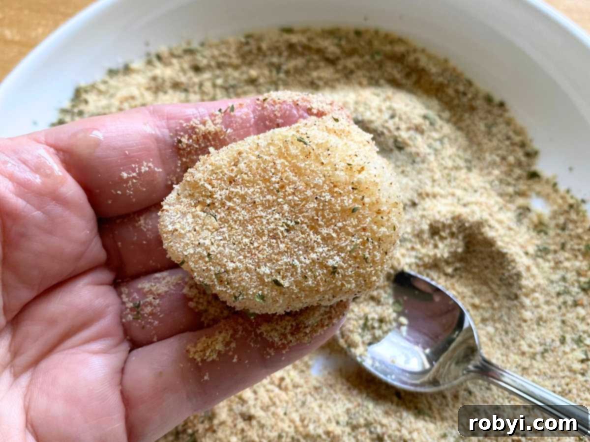 Hand holding a sea scallop lightly covered with Parmesan breading.