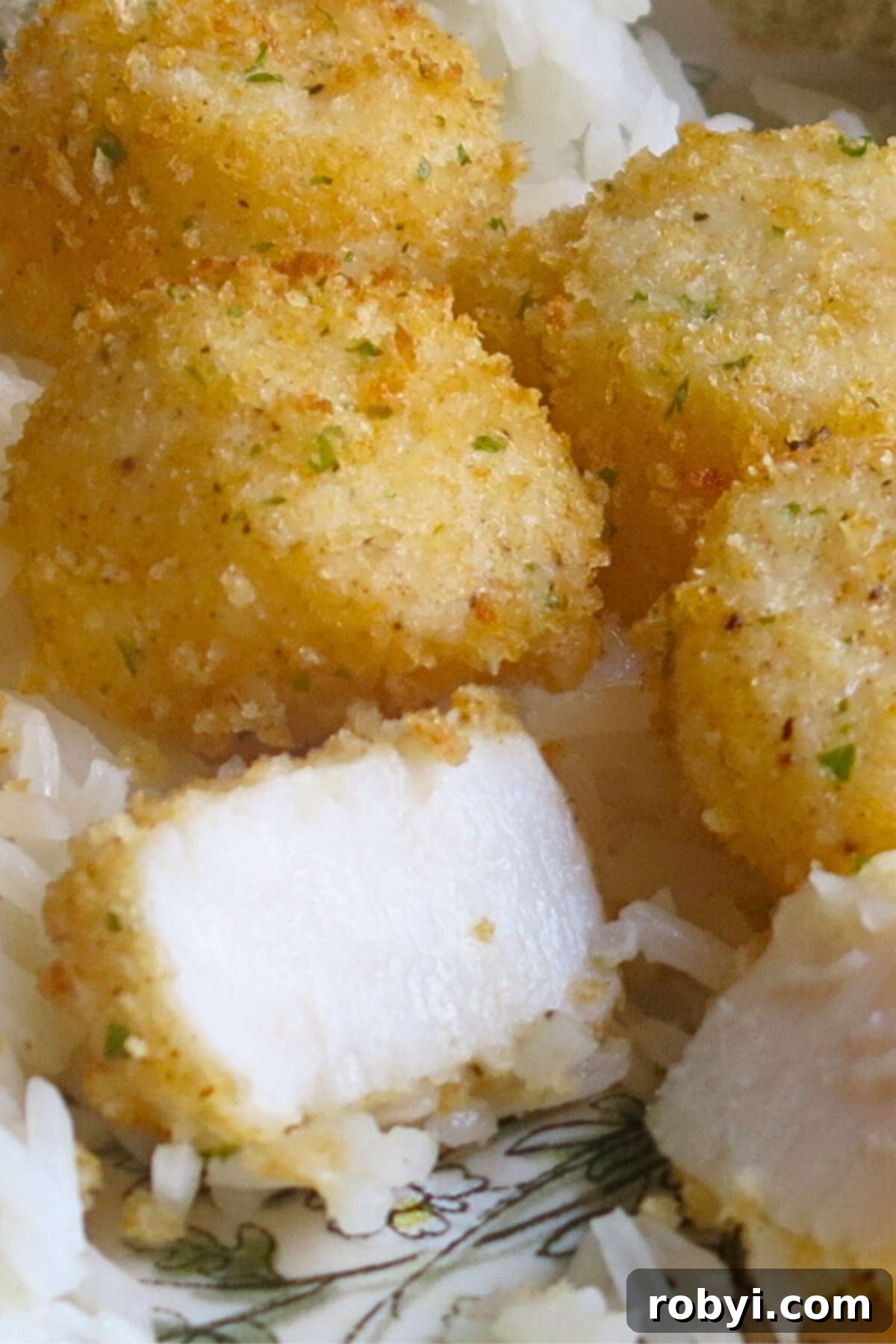 Broiled scallops with Parmesan breading on a plate over rice with one cut in half to expose the moist, white center.